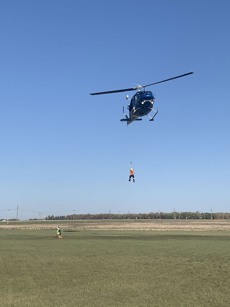 Un monteur de lignes est suspendu à un câble sous un hélicoptère en vol stationnaire.