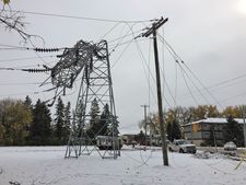 A tower is bent in half beside a hydro pole with downed lines.