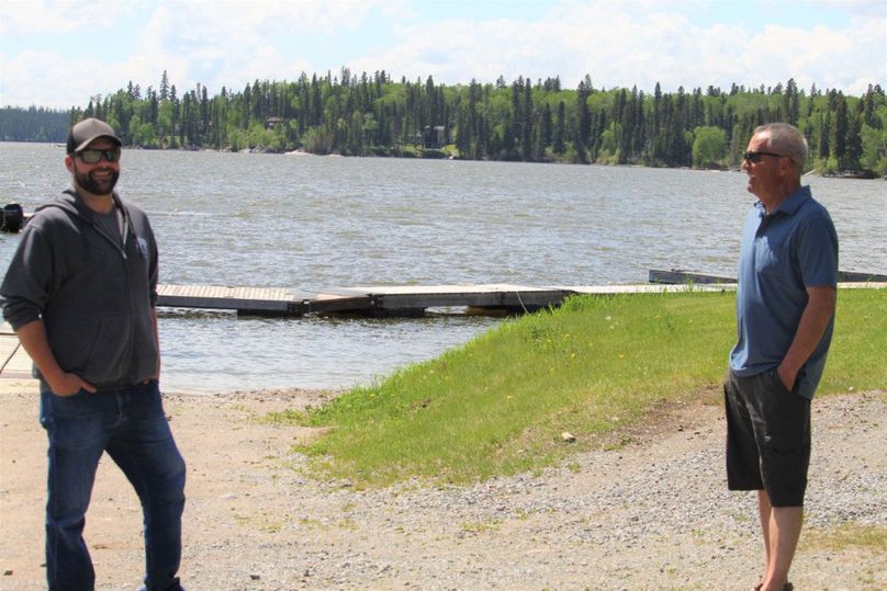 Two men stand beside each other with a lake in the background.