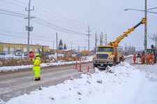 A traffic controller stops traffic while the crew sets a hydro pole. 