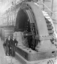 Two men stand beside a generating unit under construction.