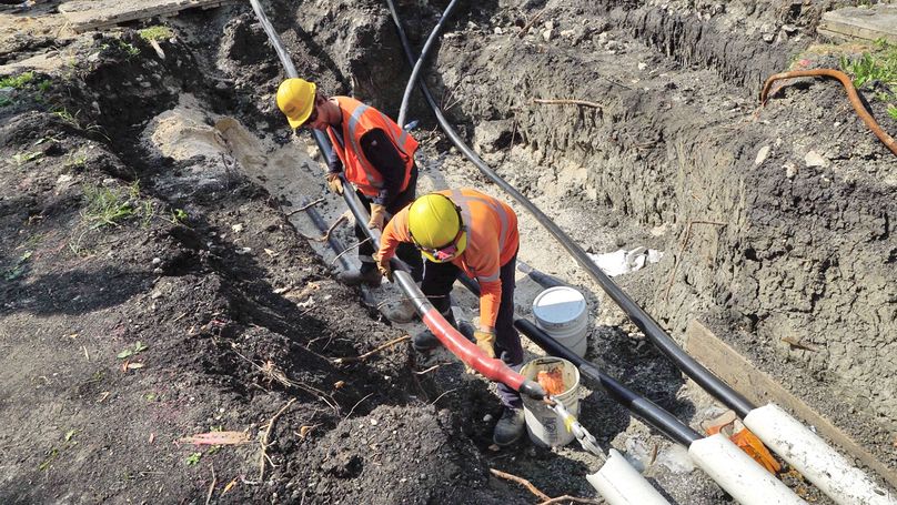 Deux travailleurs de Manitoba Hydro, debout dans une fosse, insèrent le dernier des trois gros câbles à haute tension dans une canalisation.