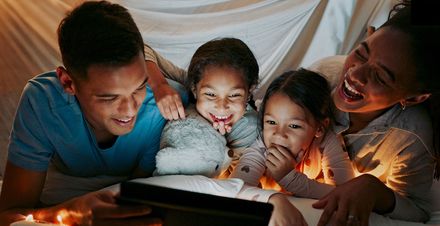 Family smiling and laughing while they watch a show together on a device.