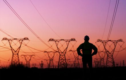 A worker looks out at hydro lines at sunset.