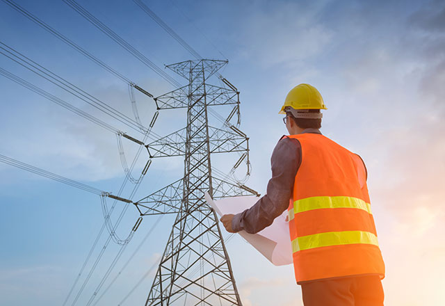 Worker holding plans under a hydro tower