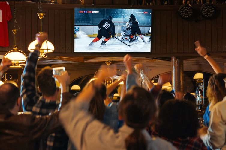 Local bar full of people cheering together while watching a hockey game on TV