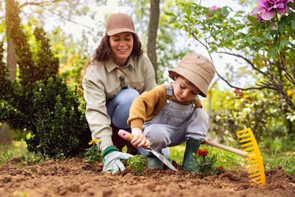 A young child helping their mother plant a flower in a flower bed.