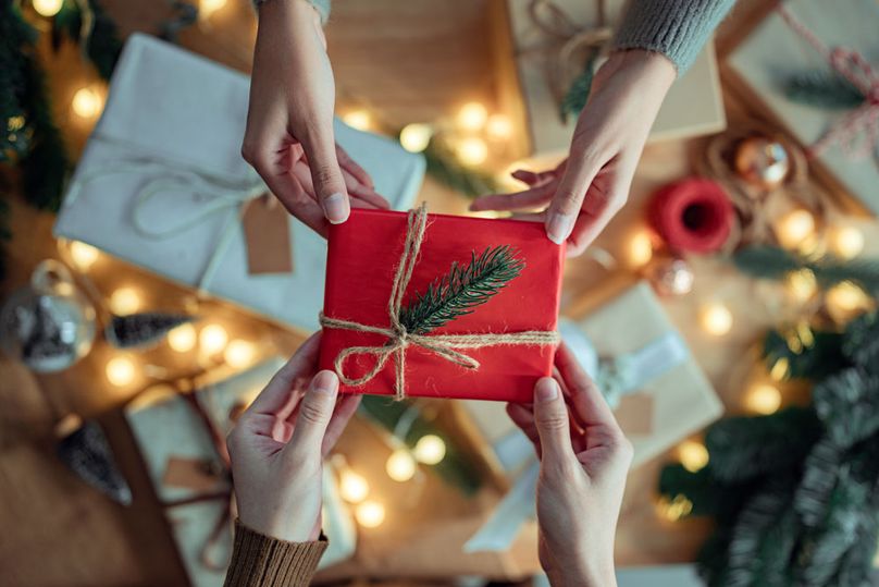 Two sets of hands hold each corner of a red, wrapped gift