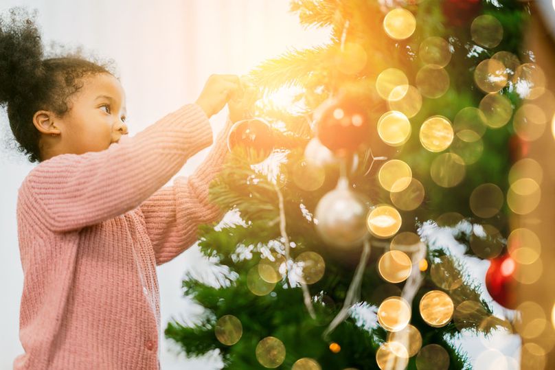 A little girl puts an ornament on lit up Christmas tree