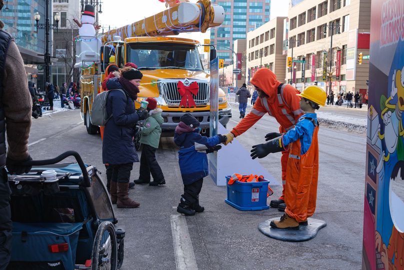 A young child reaches out to a Hydro worker standing in front of a lighted bucket truck.