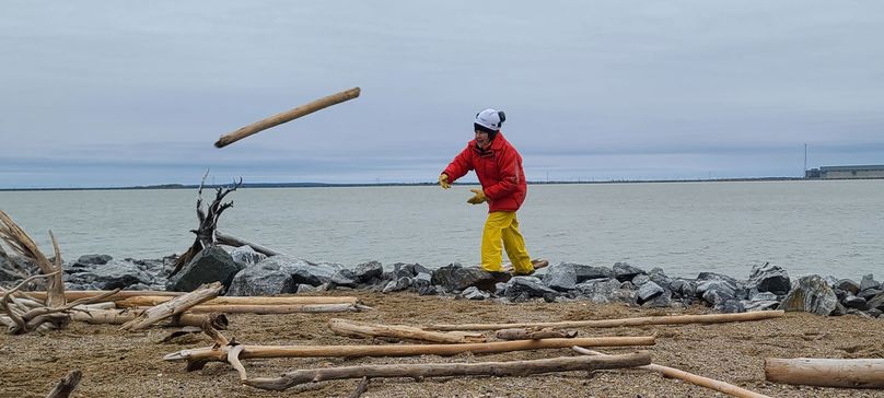 Une femme met du bois de grève en tas sur la plage de sable d’une île.