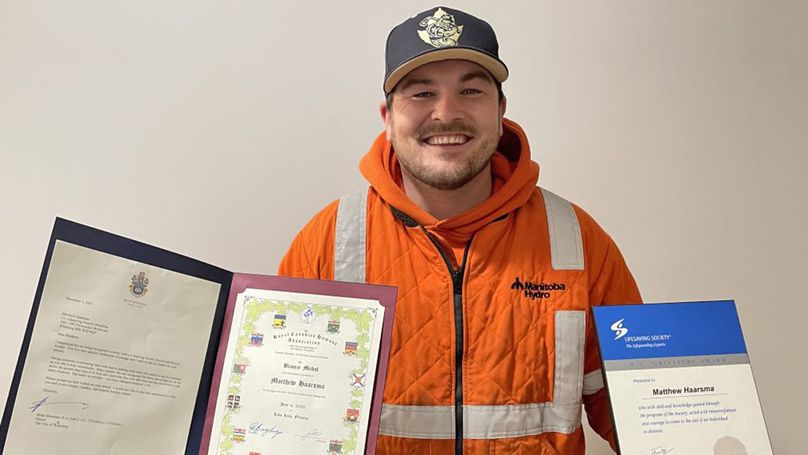 Smiling Manitoba Hydro employee holds awards received for saving a life.