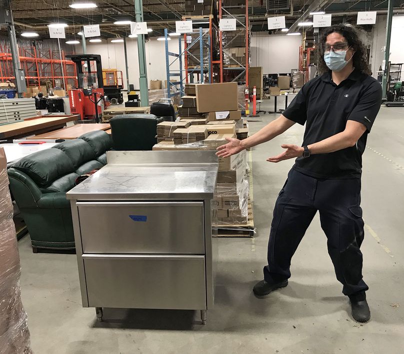 Un heureux Paul Moore montre une grande boîte à pain en métal entourée d’équipements et de meubles dans un entrepôt.