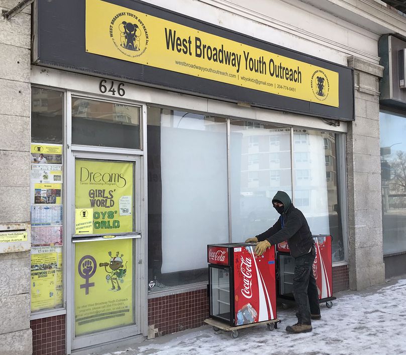 Un homme portant un masque non médical livre deux petits réfrigérateurs à la porte d’entrée du site West Broadway Youth Outreach.