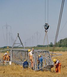 Manitoba Hydro crew in a grass field build a new bipole tower on the ground.