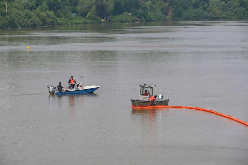 Two boats on the river with an orange boom trailing behind one boat.