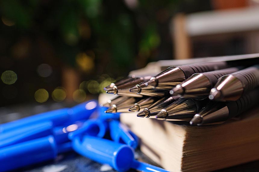 Image en gros plan de plusieurs stylos à bille sur un livre, avec leurs capuchons éparpillés au loin en arrière-plan.