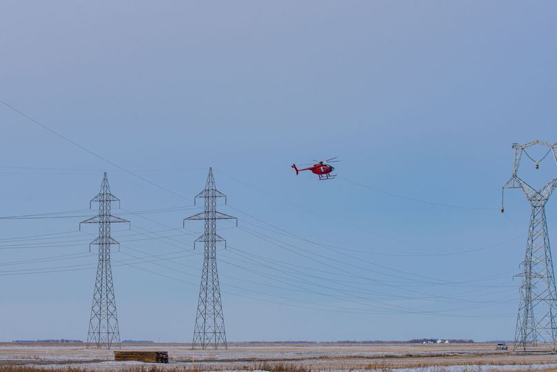 Helicopter flying cable up to pulleys at the top of a transmission tower.