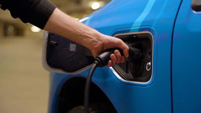A hand holds an EV charger plugged into a vehicle.