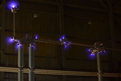 Corona discharge on energized high-voltage switch components in a dark test hall.