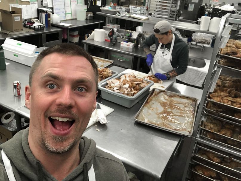 Stephen Dueck takes a selfie in commercial kitchen with chef preparing food in the background.
