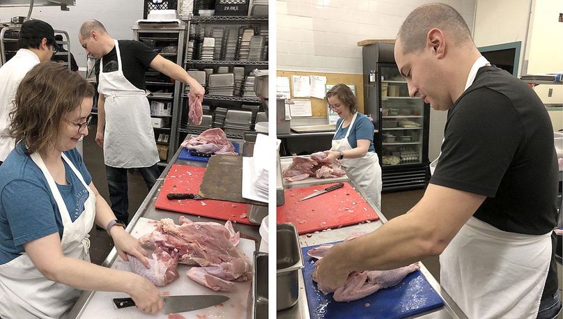 Three people cutting up raw turkey in a commercial kitchen.