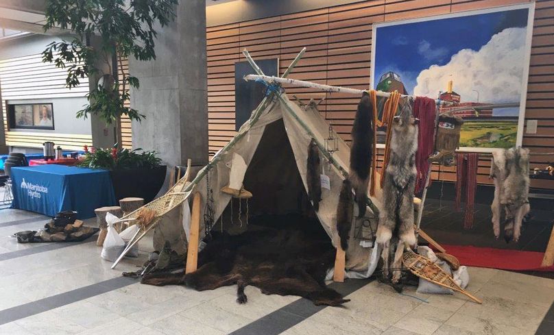 A trapper’s canvas tent is displayed in the Hydro gallery with furs hanging from birch posts, moccasins, Metis sashes, snowshoes, and cooking utensils.