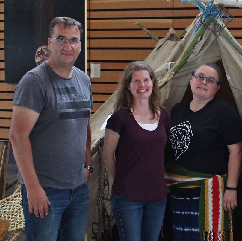 A man and two women stand in front of a trapper’s tent display.