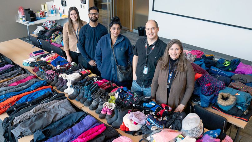 Hydro employees stand beside several tables full of folded and sorted jackets, mitts and other winter wear.