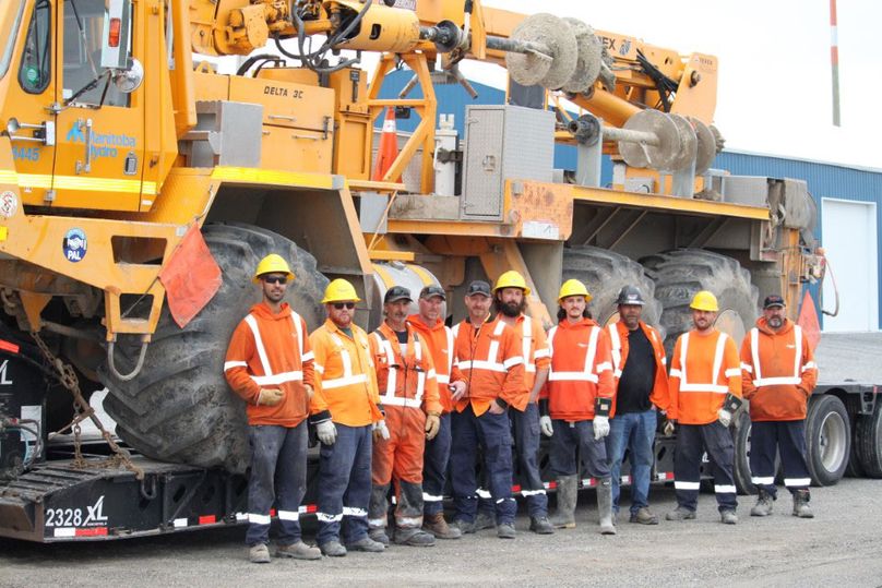 A group of people wearing personal protective equipment and standing in front of a yellow bucket truck.