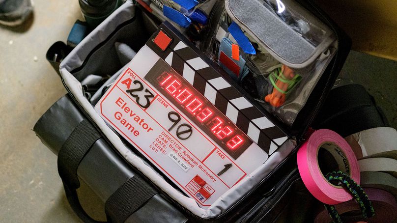 A film clapperboard for the movie “Elevator Game” sits on a camera bag.