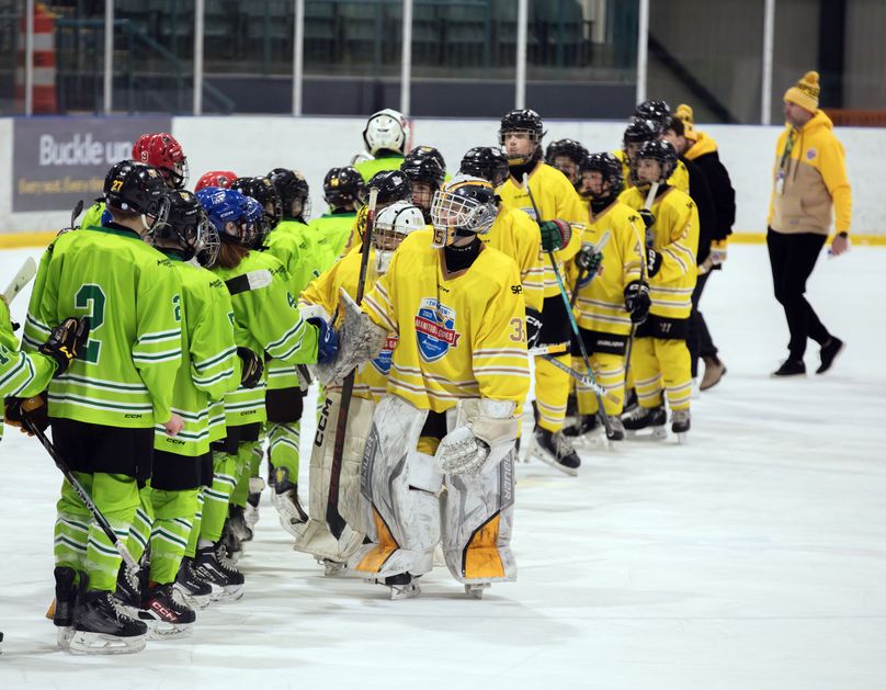 Two hockey teams line up and shake hands at centre ice.