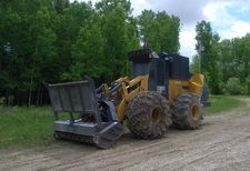 A large-wheeled yellow construction vehicle with a mulching attachment on the front used to clear vegetation along electrical infrastructure.