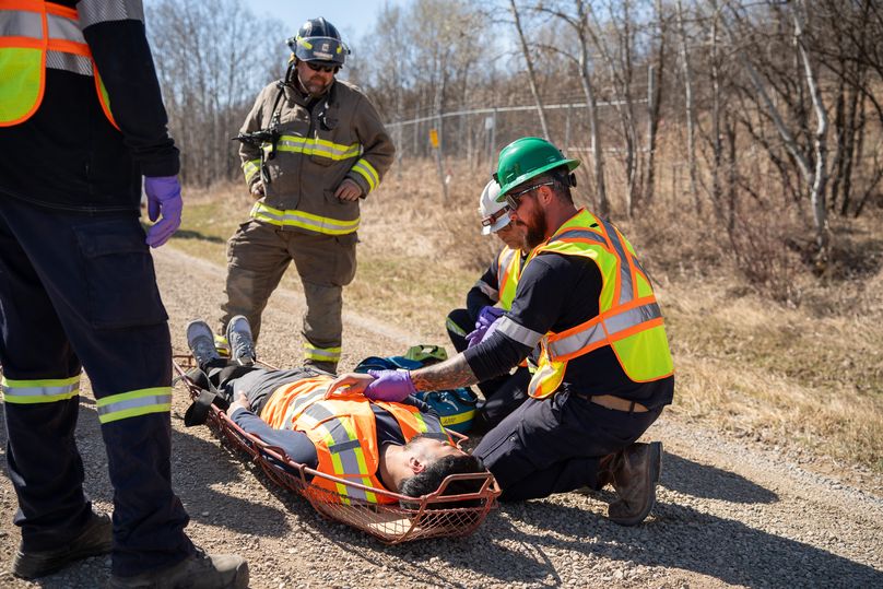 A person laying on a stretcher is surrounded by a group of people in high visibility clothing.