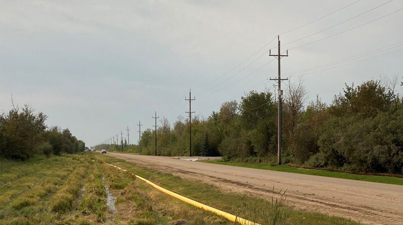 Des canalisations jaunes sont posées à côté d’un chemin de terre.
