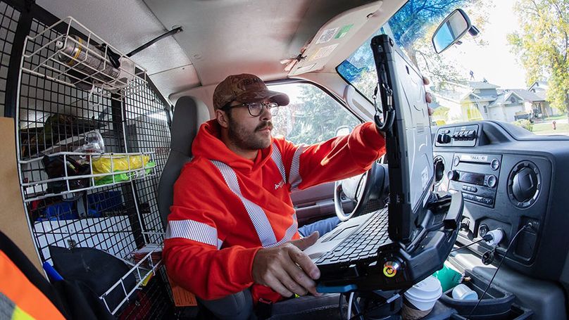 A man in high visibility clothing uses a laptop in a parked van.