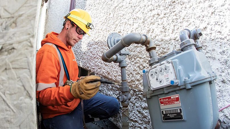A man in high visibility clothing uses a handheld monitoring device on a gas meter outside a residence.