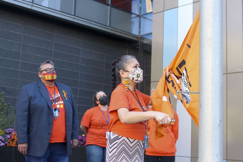 A Manitoba Hydro employee, Rose Monkman, raises an orange Every Child Matters flag up the pole.