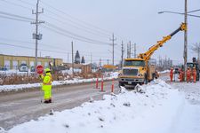 A traffic controller stops traffic while the crew sets a hydro pole.