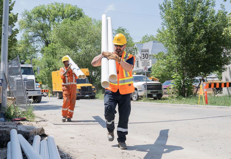 Two Manitoba Hydro workers carry pipes at the work site.
