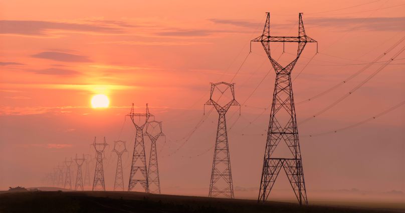 Large transmission towers carry powerlines into the sunset.