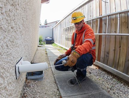 Un employé en vêtements haute visibilité examine de l’équipement de gaz naturel près d’une maison.
