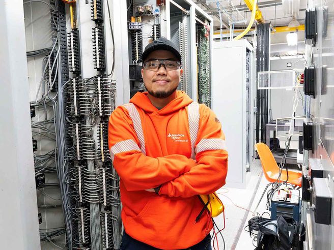 Employé de Manitoba Hydro travaillant dans une installation de télécommande, entouré d’équipements électriques et de panneaux de câblage.