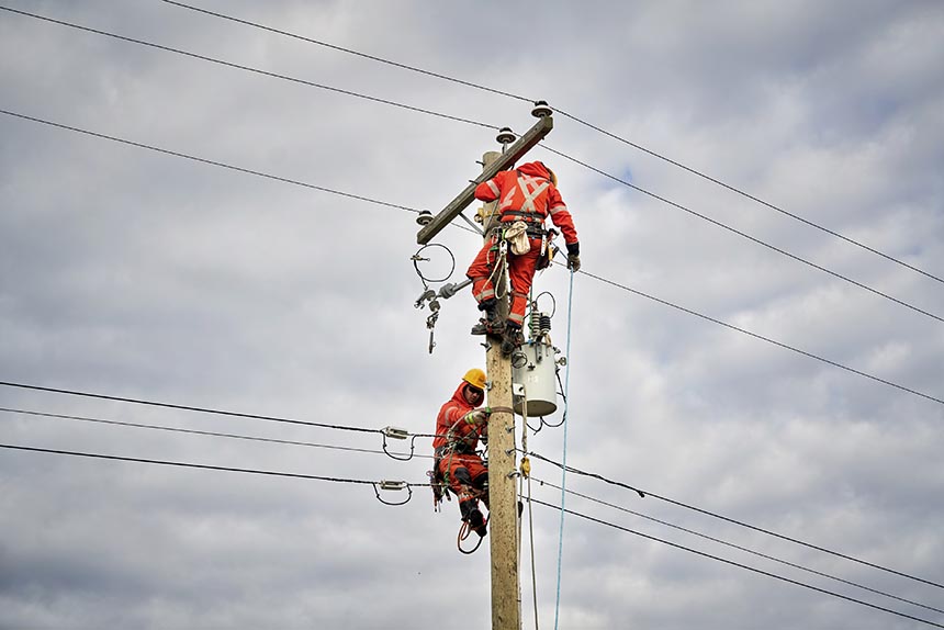 Two power line technicians working to repair lines on a hydro pole.