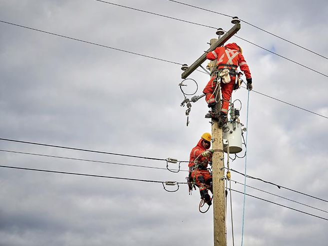 Two power line technicians working to repair lines on a hydro pole.