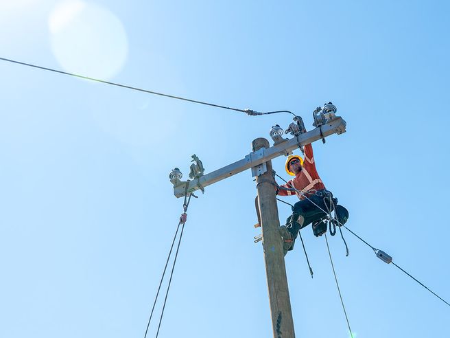Two power line technicians working to repair lines on a hydro pole.