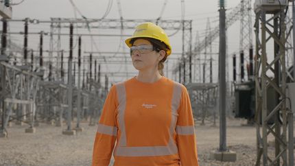 Un employé de Manitoba Hydro vêtu d’équipement de sécurité à haute visibilité se tient devant un poste de conversion.