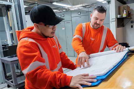 Two technicians in high-visibility clothing looking at documents.