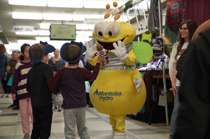 Two kids interact with a bug mascot in a yellow costume.
