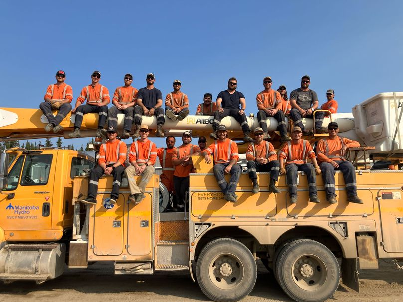 A group of SaskPower and Manitoba Hydro restoration crew members posing on a Manitoba Hydro bucket truck.